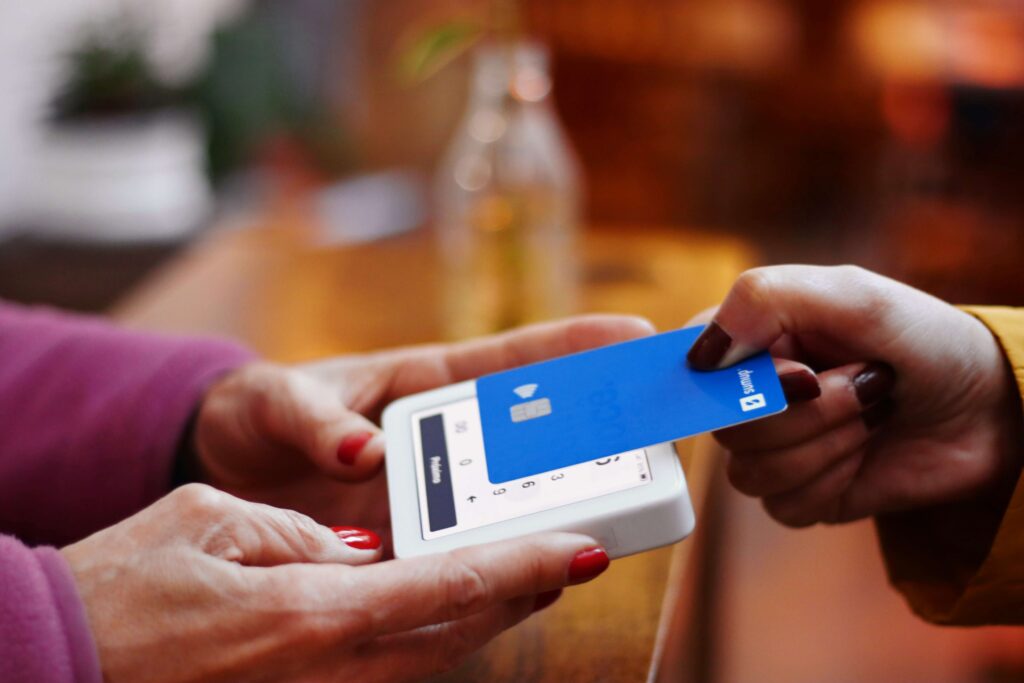 A person tapping a blue contactless credit card on a portable card reader, representing digital payments, contactless transactions, and secure payment processing