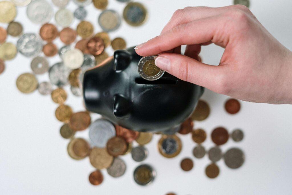 A hand dropping a coin into a blue piggy bank, symbolizing financial savings