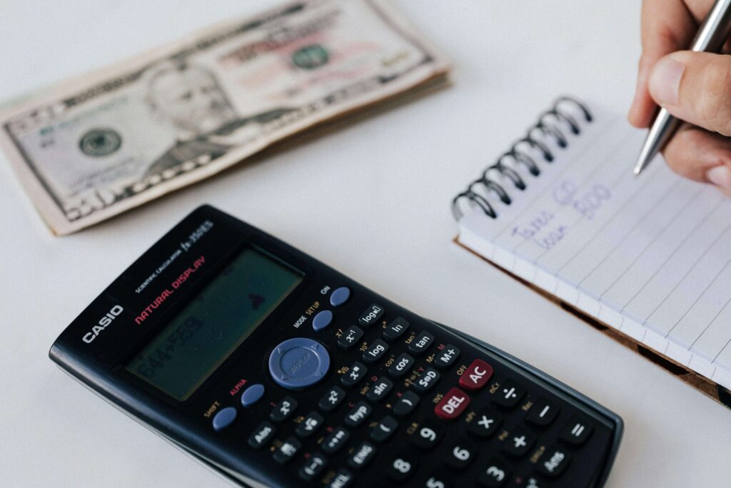 Hand writing financial notes while using a calculator, planning budgeting strategies, and managing personal finances