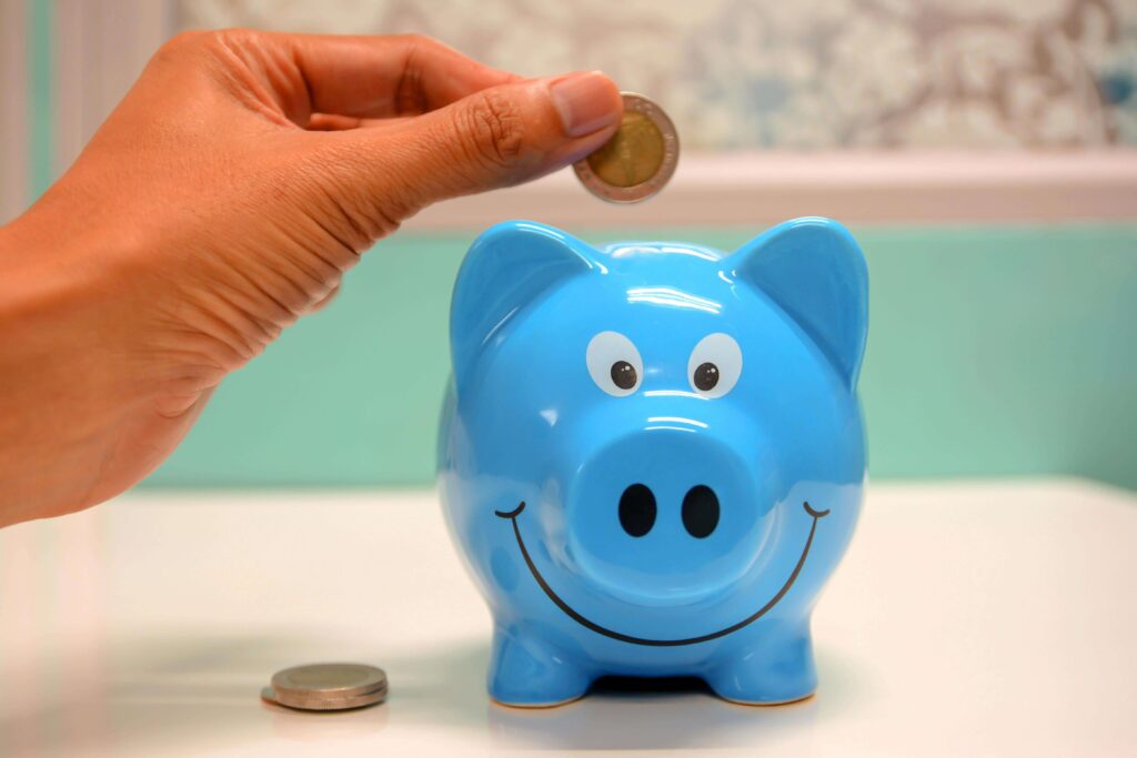 A hand dropping a coin into a blue piggy bank, symbolizing financial savings, budgeting, and money management