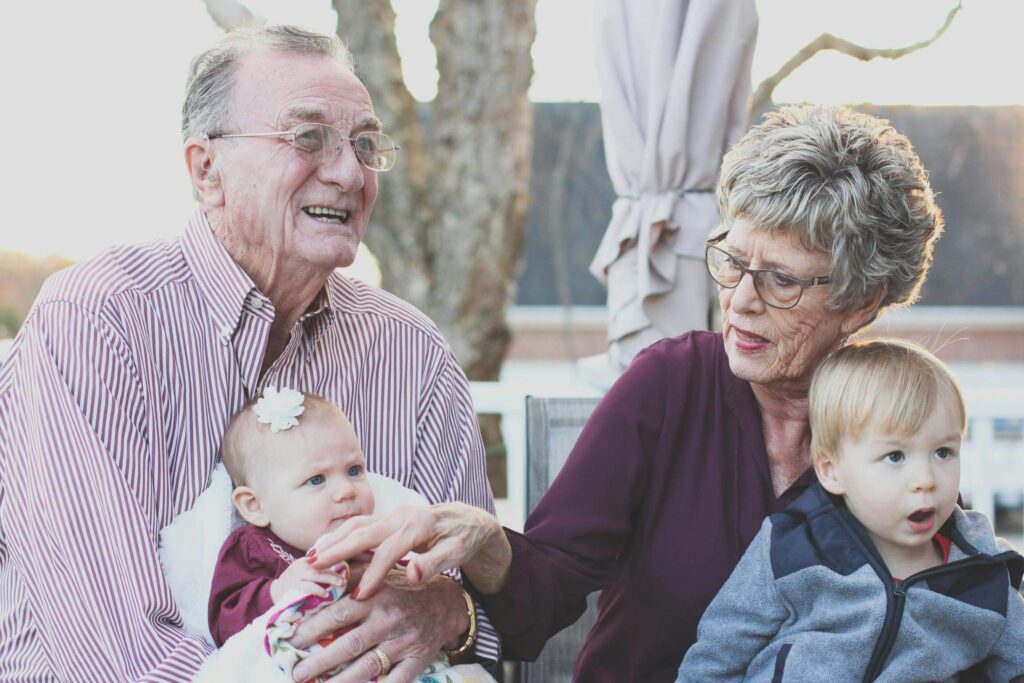 An elderly couple sitting outdoors with their grandchildren, symbolizing family bonding, generational relationships, and spending quality time together