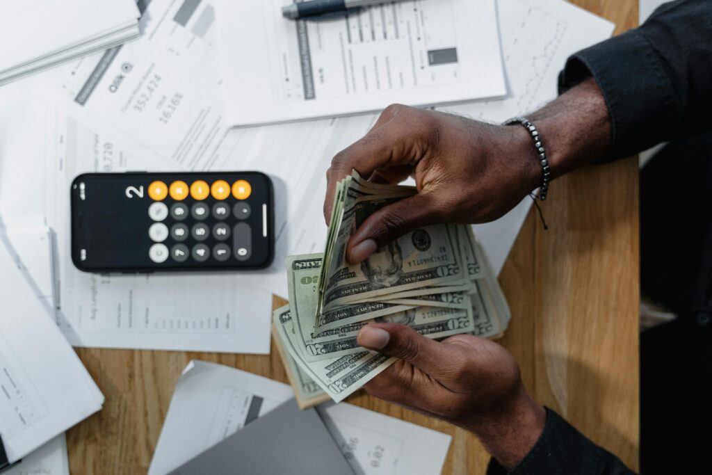 A person counting dollar bills at a desk with a calculator and financial documents, representing budgeting and cash management